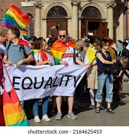 Cracow, Poland - May 2022: A a rainbow flag wrapped on a man with sunglasses behind a white banner with lettering "Equality" on an LGBT parade for equality at the Main Market Square. Selected focus.