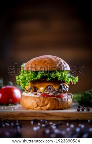 Craft beef burger with cheddar, bacon, lettuce and sauce on wooden background