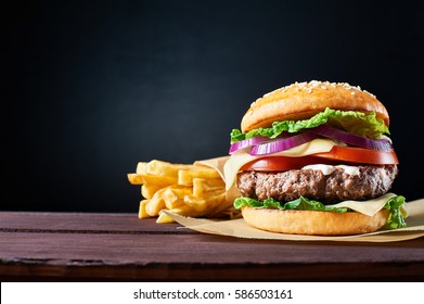Craft beef burger and french fries on wooden table isolated on black  background.