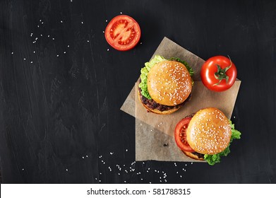 Craft beef burgers with vegetables. Flat lay on black textured background with sesame seeds.