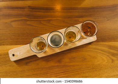 Craft Beer Tasting Flight Of Pints Served On Paddle On Wood Table Top Down View