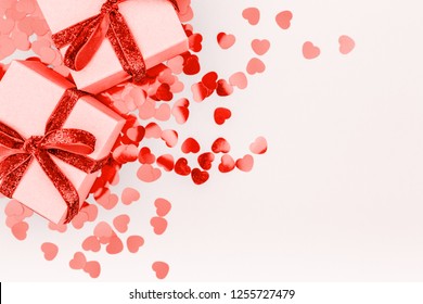 Craft boxes with red ribbon bow and glitter heart confetti. Valentine day concept. Trendy minimalistic flat lay design background. Horizontal. Living coral theme - color of the year 2019