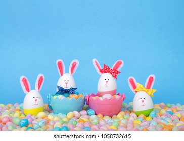 Craft Easter Bunnies made from plastic eggs Two in baskets full of candy with two standing in pastel jelly beans with a light blue background. Fun Easter line up with copy space