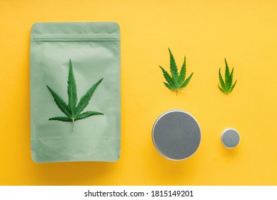 Craft Green Package With Cannabis Leaf And Metal Jars. Different Sizes Of Cannabis Packages, Weed Trade Legalization. Pharmacy Drugs Medical Marijuana On Yellow Background