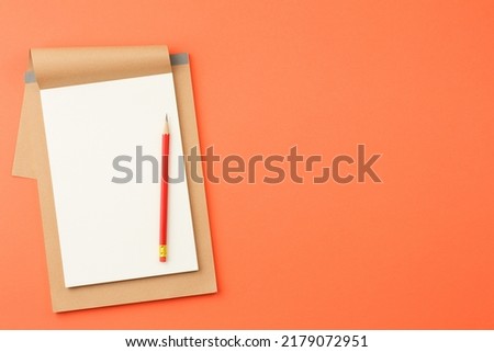 Craft notebook with white sheets, red pencil on orange isolated background top view.