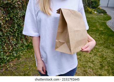 Craft Paper Bag In The Hands Of A Girl. Gift Wrapping. Food Delivery Service. Paper Bag Close Up. Cardboard Case. Blank Space Mockup For Design, Lettering Or Advertising