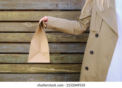 Craft Paper Bag In The Hands Of A Girl. Gift Wrapping. Food Delivery Service. Paper Bag Close Up. Cardboard Case. Blank Space Mockup For Design, Lettering Or Advertising