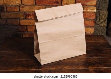 Craft Paper Bag On A Wooden Table Against A Brick Wall. Takeaway Food Packaging Rustic Template