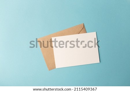 Craft papper envelope and white card on isolated pastel blue background.