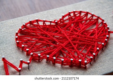 Craft String Art In Shape Of Heart. Red Woolen Heart, Symbol Of Love, Made Of Red Wool Yarn Threads Tangled Over Metal Nails On Canvas Background