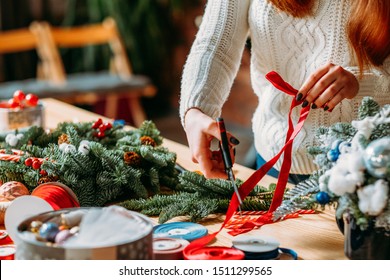 Craft Workshop. Cropped Shot Of Female Florist Using Red Ribbon, Green Fir Tree Twig To Create Christmas Interior Decoration.