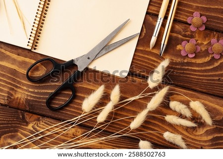 Crafting project setup with scissors, notebook, and decorative materials on wooden table