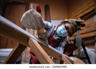 Craftsman, Carpenter Using A Paintbrush Painting To Wooden Bar Chair Handmade At Woodworking Workshop Or Carpentry Workplace. Selective Soft Focus On The Paintbrush.