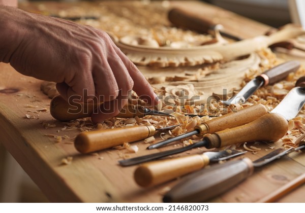 Craftsman carving with\
a gouge. Woodwork. Workbench with equipment. Wood carving tools.\
Chisels for carving