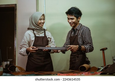 craftsman and craftswoman wearing a hijab make a leather belt in a leather workspace - Powered by Shutterstock