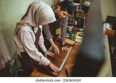 craftsman and craftswoman wearing hijab using a ruler measuring leather patterns in a leather workspace - Powered by Shutterstock