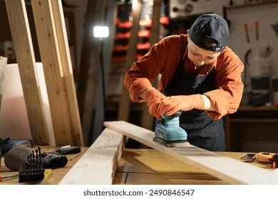 Craftsman and DIY handmade. Female carpenter using electric sander in carpentry workshop, sanding wooden planks. Copy space - Powered by Shutterstock