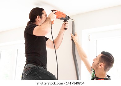 Craftsman Drills Hole In A Wall With Impact Drill And His Apprentice Assists Him In The Living Room