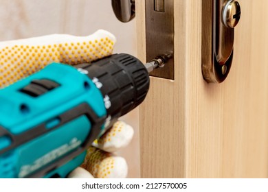 A Craftsman With An Electric Screwdriver In His Hands Inserts A Lock Into The Door. Tighten The Screw In The Door Lock