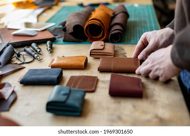 Craftsman hands laying out exclusive leatherwork on wooden table at leather workshop. Male tanner preparing handwork stuff accessories to sending clients or making promotional photo for advertising - Powered by Shutterstock