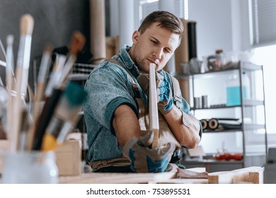 Craftsman holding wooden board and checking quality while working at home carpentry