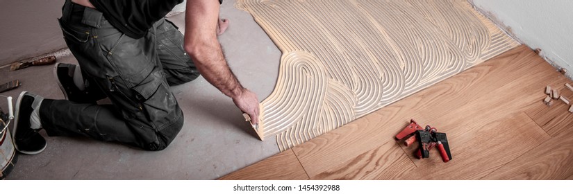Craftsman lays parquet floor and spreads the glue on the screed and beats the floorboards with the hammer and the block