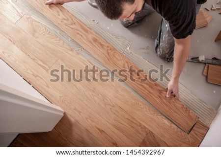 Craftsman lays parquet floor and spreads the glue on the screed and beats the floorboards with the hammer and the block