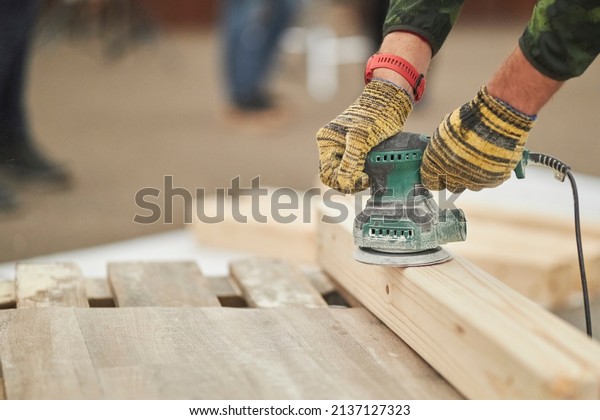 craftsman polishes a solid wood board with a\
sander, furniture restoration. The polished wood working. Close up\
of sanding a wood with orbital\
sander