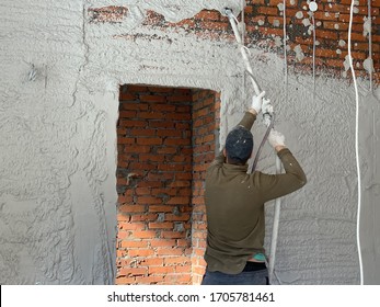 The Craftsman Puts The Plaster On A Brick Wall. The Builder Is Engaged In Wall Cladding. The Painter - The Plasterer Works With A Spray Gun.