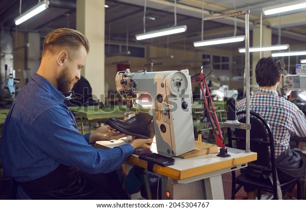 Craftsman shoe designer repairing or sewing boot\
on industrial stitching machine. Footwear making process. Side view\
shot. Handyman shoemaker working at workplace checking item on\
defect
