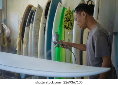 Craftsman surfboard working in a repair workshop, man spray painting a surfboard. - Powered by Shutterstock