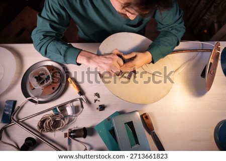 Craftsman upcycle master disassembling vintage electric lamp at workshop, man preparing item parts for repairing and inspection, taking out light bulb socket off lampshade, refurbishing and reuse.
