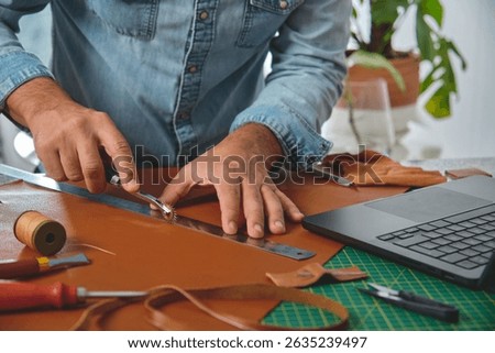Craftsman using stitching groover and ruler on leather in his workshop, small business and entrepreneurship concept