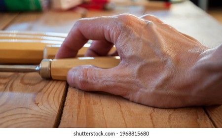 Craftsman's Strong Hand On Wooden Table Holding A Wood Carving Gouge.