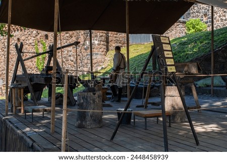 Craftsman's yard, designed in the style of a historical epoch. Blacksmith shop. Coin minting. A figure in a historical blacksmith costume, turned away. The Golden Horde city of Ukek in Vyborg.