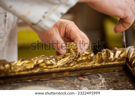 Craftsmanship, craftsman. Restoration of an antique gilded frame, hands at work in the foreground.
