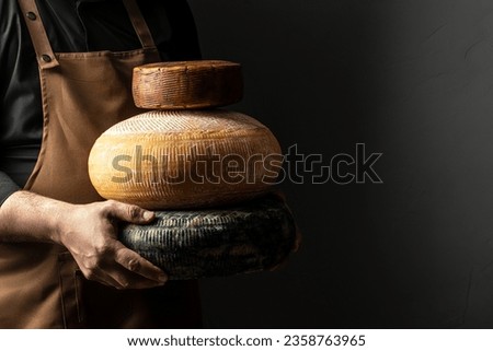 craftsmanship hands have a typical Italian cheese. French tomme cheese in the hands of a cheesemaker on dark background. Long banner format.
