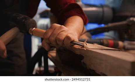 Craftsperson carving into wood using chisel and hammer in carpentry shop with precision. Manufacturer in studio shaping wooden pieces with tools, making wood art, camera B close up shot - Powered by Shutterstock