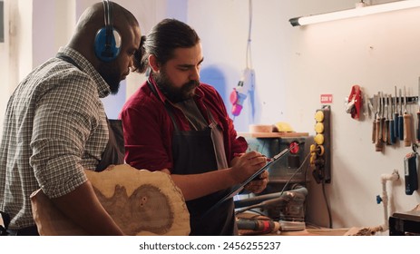 Craftsperson and colleague look over technical schematics to make commissioned wooden object. Manufacturer and coworker analyze blueprints to execute furniture assembling woodworking project, camera A - Powered by Shutterstock