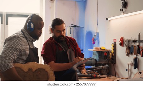 Craftsperson and colleague look over technical schematics to make commissioned wooden object. Manufacturer and coworker analyze blueprints to execute furniture assembling woodworking project, camera B - Powered by Shutterstock