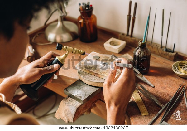 Craftsperson making jewelry design using flame\
torch and tool in the workshop. Jeweler working at work desk with\
traditional tools in her\
studio.