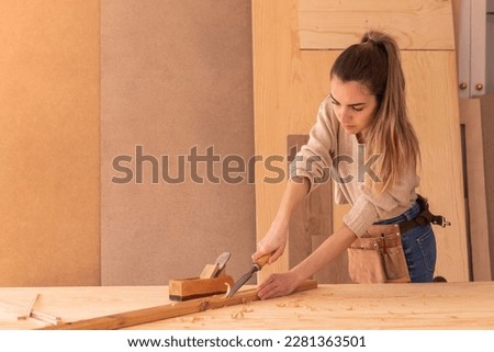 Craftswoman carving wood with chisel. Concentrated female joiner in apron gouging wood with chisel near jack plane