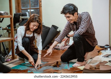 craftswoman cuts leather guided by a male craftsman in workshop - Powered by Shutterstock