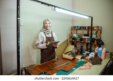 craftswoman in hijab smiling at camera while using pad in leather workshop - Powered by Shutterstock