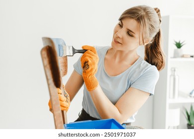 Craftswoman wearing gloves is carefully painting an old wooden chair in blue. She seems to be happy doing some diy work at home - Powered by Shutterstock