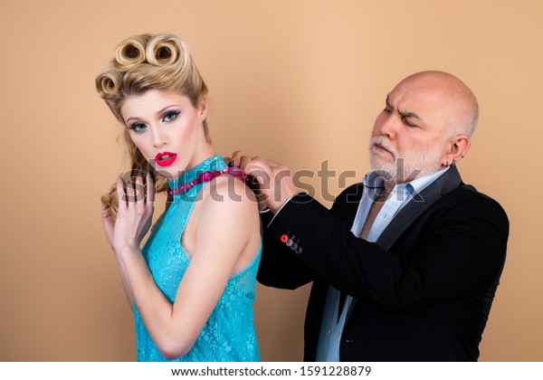 Crafty blonde woman want to
marry rich sugar daddy to get his money. Difference of ages
concept. Couple of younger woman and elder man isolated at orange
background