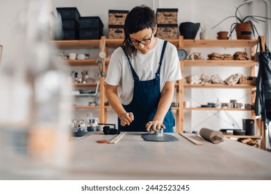 A crafty creative artist is molding wet clay at her ceramics studio. Portrait of a young craftswoman creating clay artwork at pottery workshop. A female ceramist is designing ceramics and pottery. - Powered by Shutterstock