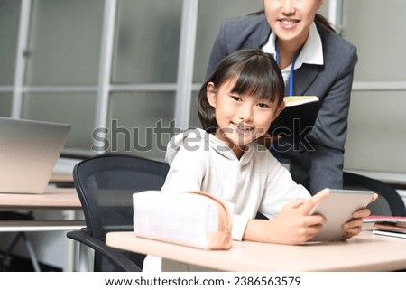 A cram school instructor teaches an elementary school girl how to use a tablet in the classroom.
