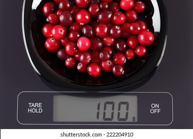 Cranberries in a black plate on digital scale displaying 100 gram.