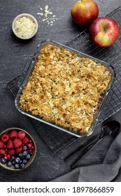 Cranberry And Apple Crumble, Crisp In A Glass Baking Dish With Almond Flakes And Fresh Berries On Dark Stone Concrete Background. Top View.